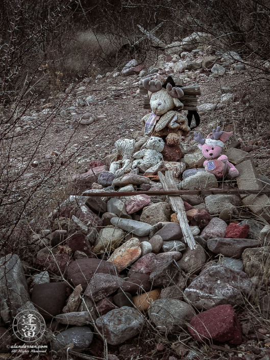 Stone cairn bedecked with weathered stuffed animals.