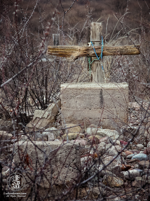 Wooden cross grave marker draped with torquoise rosary.