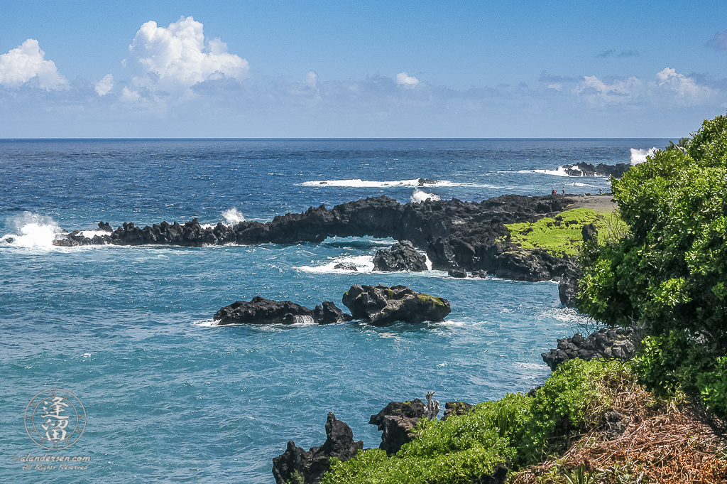 Black lava bridge arching out over the blue ocean waters at Waianapanapa State Park.