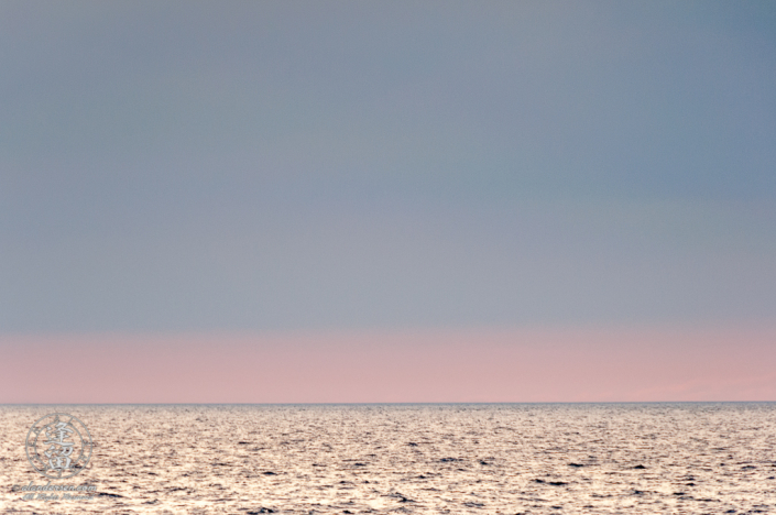 Pastel pink and blue evening sky merging into gray waters of the ocean at the horizon.