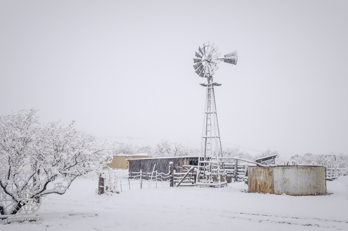 Thick snow blanketing windmill and corrals