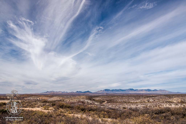Cirrus clouds streaking over desert mountain range.