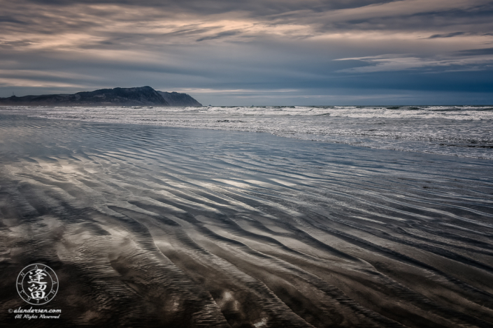Rippled wet sand reflecting storm clouds from overcast sky at Del Rey Beach State Recreation Site, Oregon.