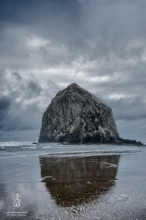 Haystack Rock reflected in the wet sand on cloudy and stormy day.