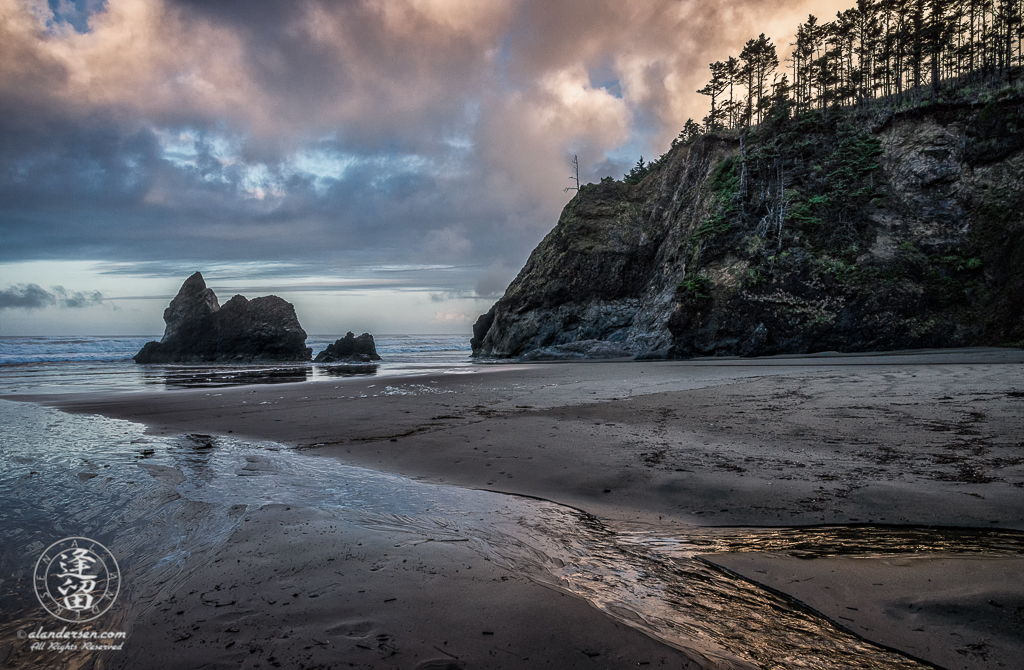 Lion Rock and sky reflections at Sunrise in the wet rippled beach sands of Arcadia Beach State Recreation Site in Oregon.