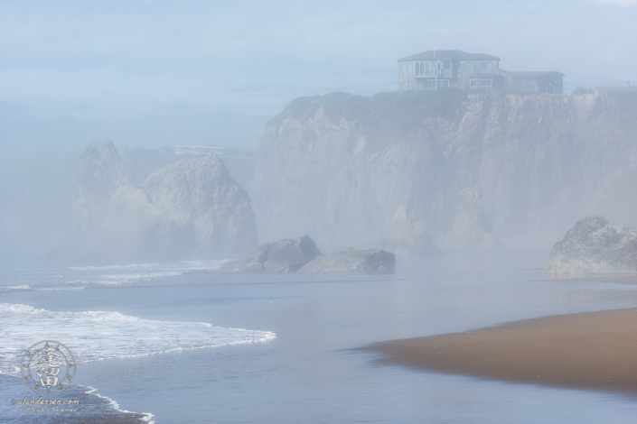 House atop cliffs seen through afternoon mists from beach near Face Rock State Scenic Viewpoint in Bandon Oregon.