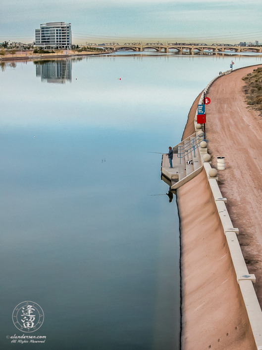 Lone urban fisherman angling from river bank.