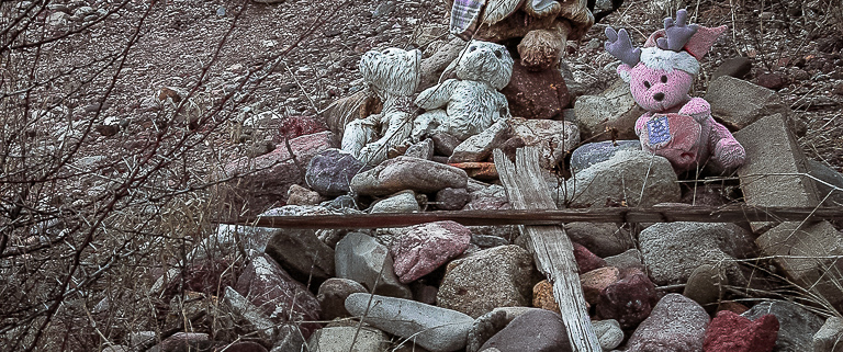 Stone cairn bedecked with weathered stuffed animals.