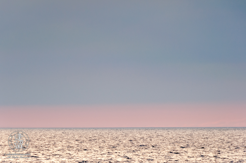 Pastel pink and blue evening sky merging into gray waters of the ocean at the horizon.