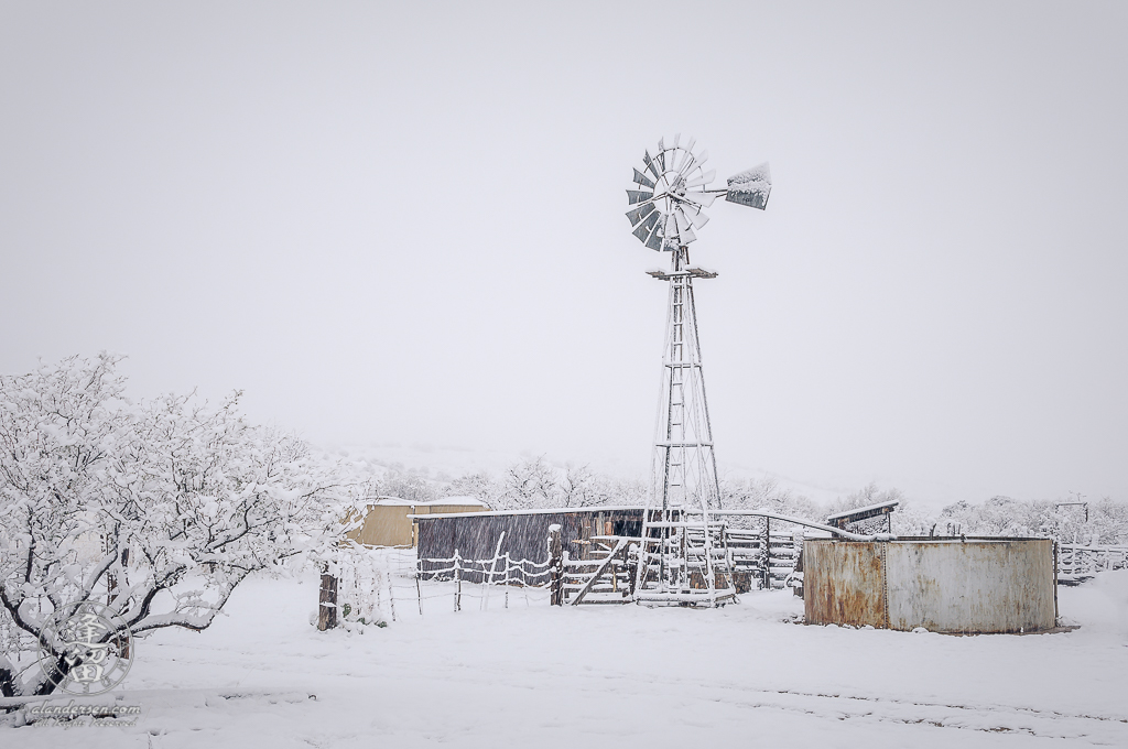 Thick snow blanketing windmill and corrals