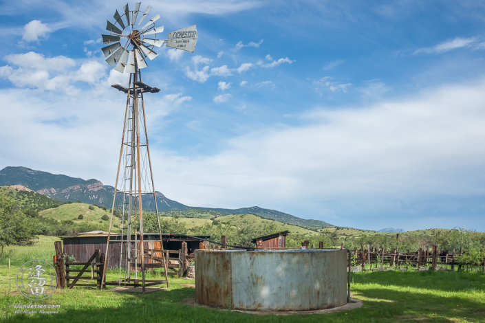 Windmill, corrals, and rolling grassy hills.