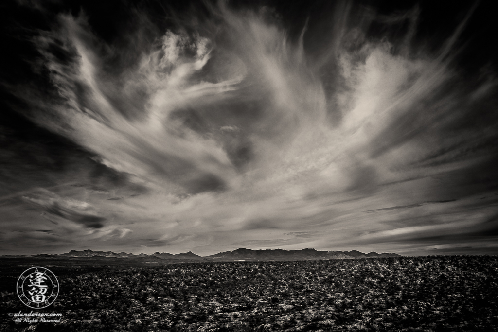 Cirrus clouds streaking over desert mountain range.