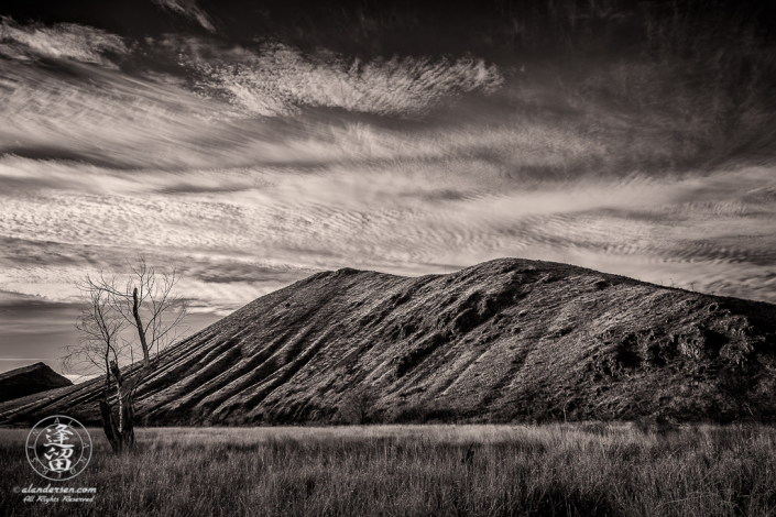 Cirrocumulus clouds looming over eroded hills and grasslands.