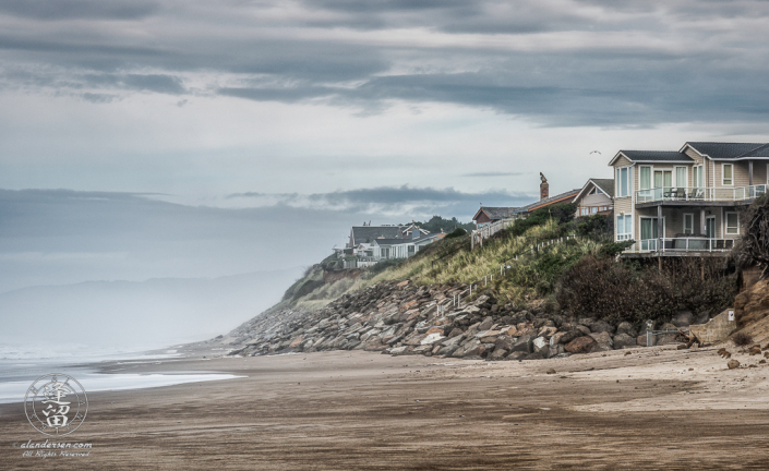 Homes line crumbling sandstone cliffs along sandy beach above Gleneden Beach State Wayside Park in Oregon.