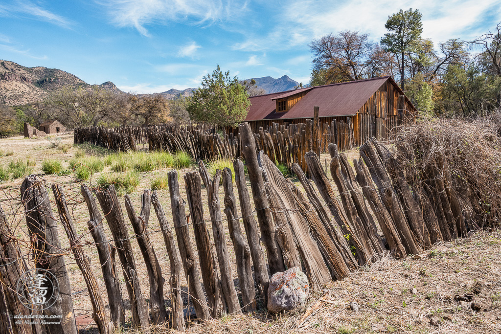 Stockaded barn surrounded by wire-woven log fence at historic Camp Rucker with adobe ruins in the distance.