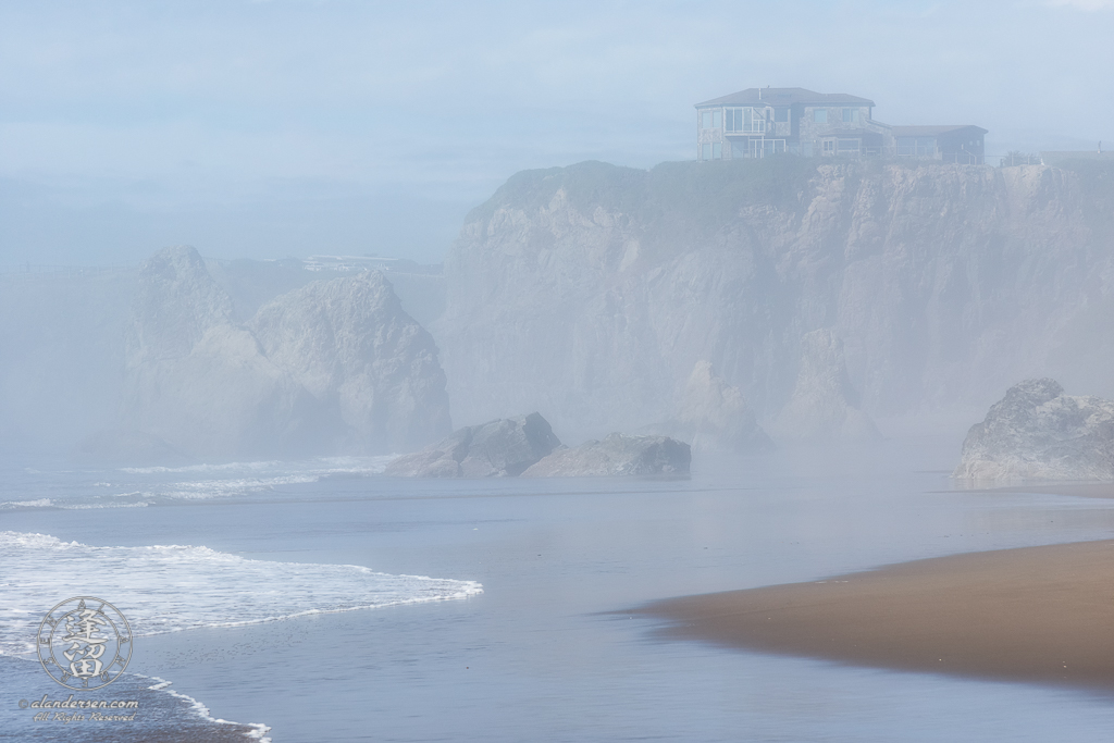 House atop cliffs seen through afternoon mists from beach near Face Rock State Scenic Viewpoint in Bandon Oregon.