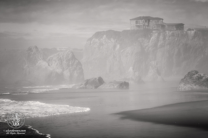 House atop cliffs seen through afternoon mists from beach near Face Rock State Scenic Viewpoint in Bandon Oregon.